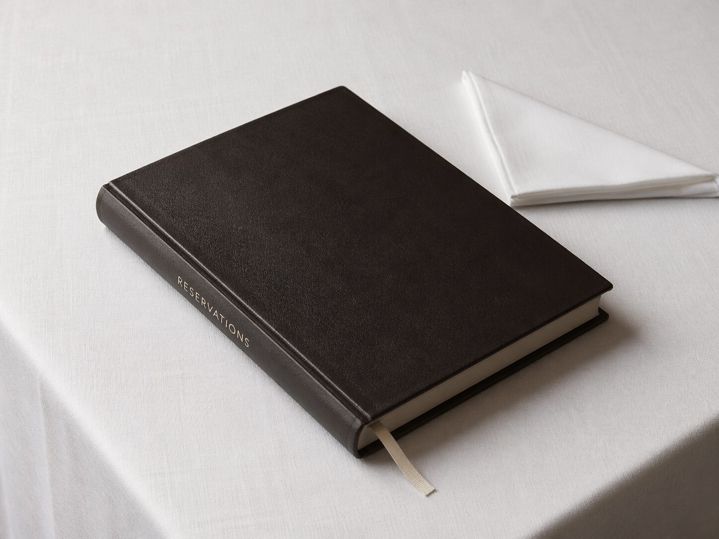 A single leather-bound reservation book closed on pressed white linen, folded napkin beside it